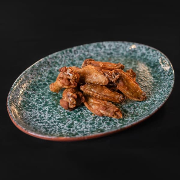 Crispy fried chicken wings piled on a speckled green and brown oval plate against a dark background.