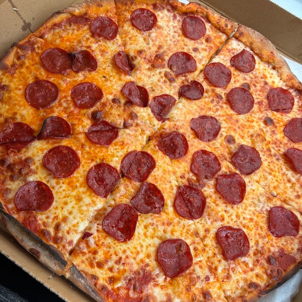 A large, round pepperoni pizza with melted cheese and a crispy crust, sliced in a cardboard box.