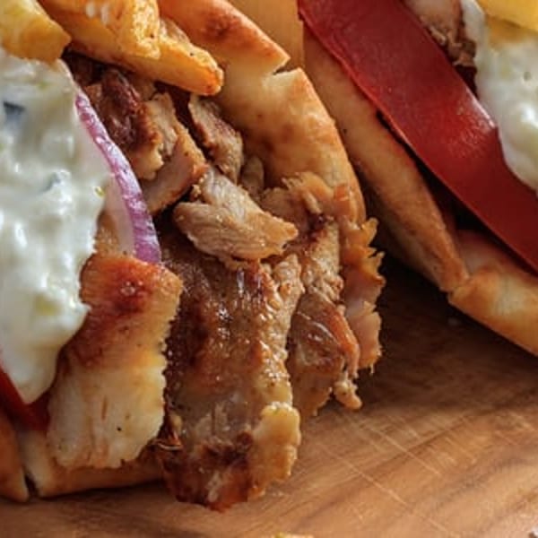 Two Greek gyros with meat, tomatoes, red onions, tzatziki sauce, and fries on a wooden board.