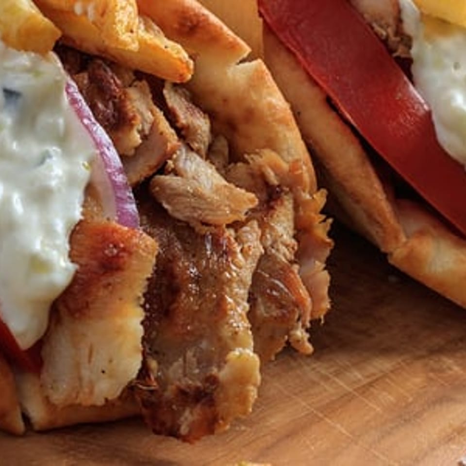 Two Greek gyros with meat, tomatoes, red onions, tzatziki sauce, and fries on a wooden board.