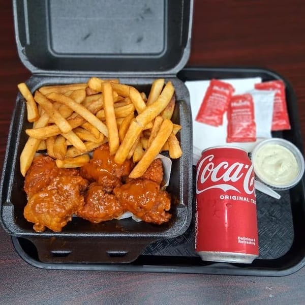 A takeout container with buffalo wings and fries, a Coca-Cola can, and dipping sauces on a tray.