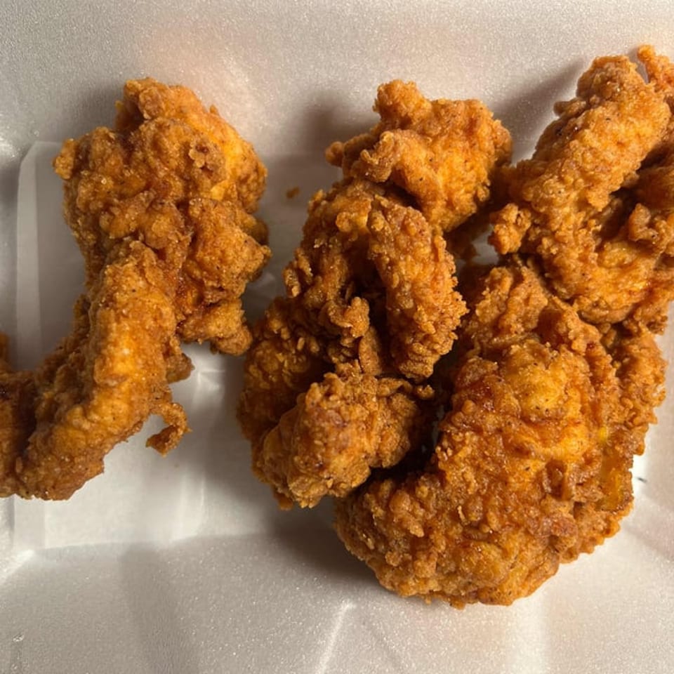 Crispy, golden-brown fried chicken tenders in a white takeout container.